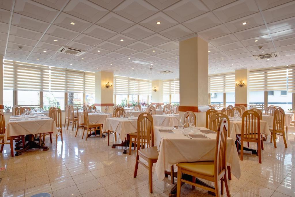 une salle à manger avec des tables et des chaises blanches et des fenêtres dans l'établissement Hotel Jalisco, à Lido di Jesolo