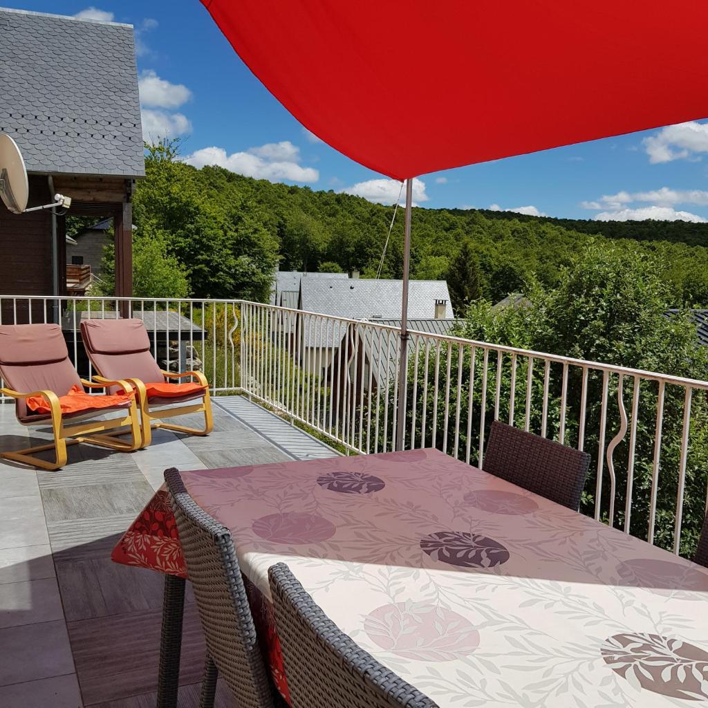 d'une table et de chaises sur un balcon avec un parasol rouge. dans l'établissement AUBRAC brameloup, à Prades-dʼAubrac