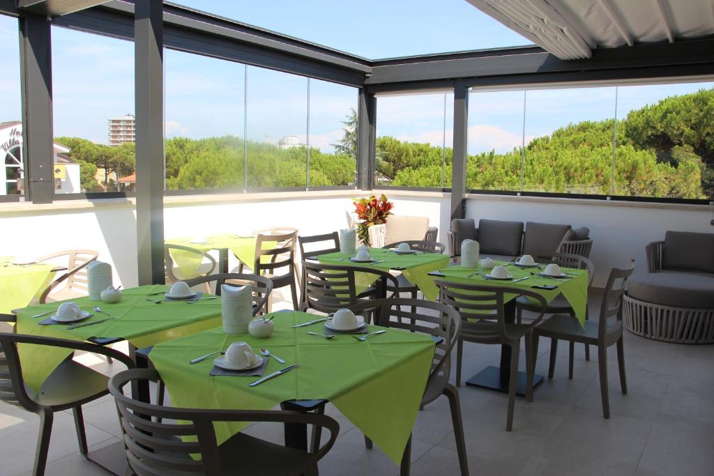 un restaurant avec des tables vertes, des chaises et des fenêtres dans l'établissement Hotel La Pigna, à Lignano Sabbiadoro