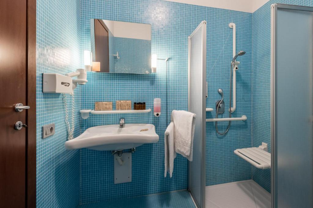 une salle de bain carrelée bleue avec un lavabo et une douche dans l'établissement Hotel Katja, à Bibione