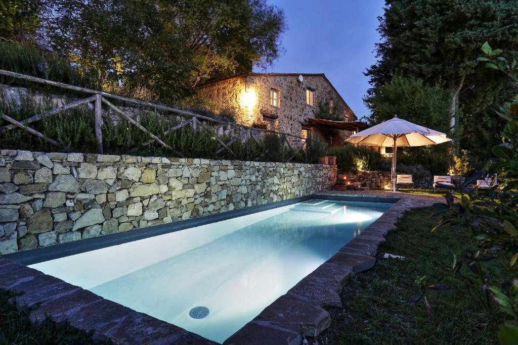 - une piscine avec un mur en pierre et un parasol dans l'établissement Villa Delle Upupe 8, Emma Villas, à Castellina in Chianti