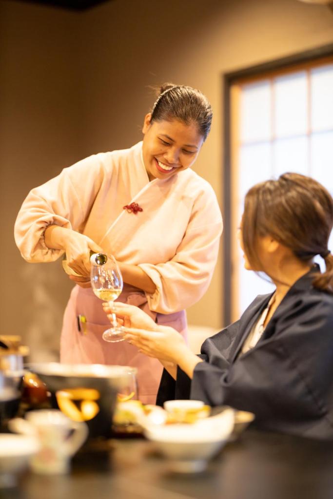 une femme versant un verre de vin à une femme dans l'établissement Komatsuya Hachinobou, à Izunokuni