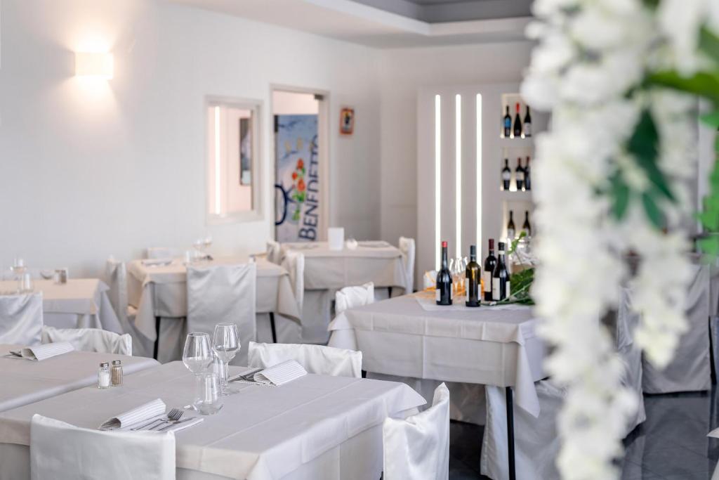 - un restaurant avec des tables blanches, des chaises blanches et des bouteilles de vin dans l'établissement Hotel Tre Rose, à Caorle