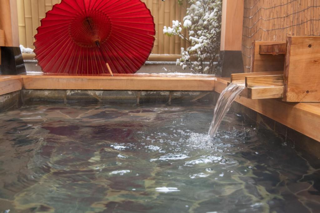 un étang avec un parapluie rouge et une fontaine dans l'établissement Ichinomatsu Japanese Modern Hotel, à Takayama