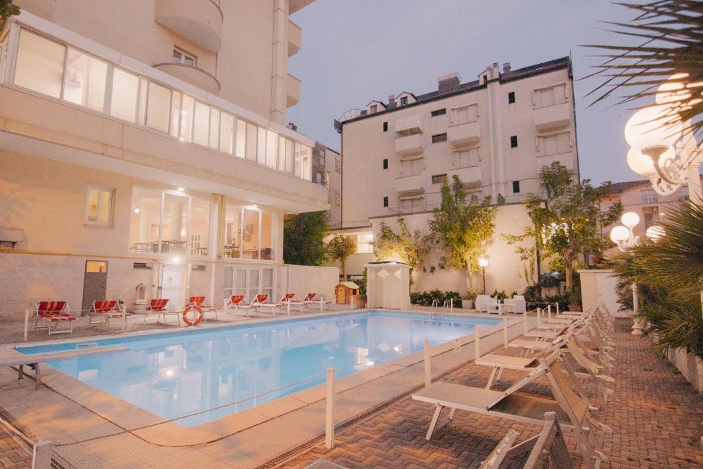 une piscine avec des chaises et un bâtiment dans l'établissement Hotel Beverly, à Rimini