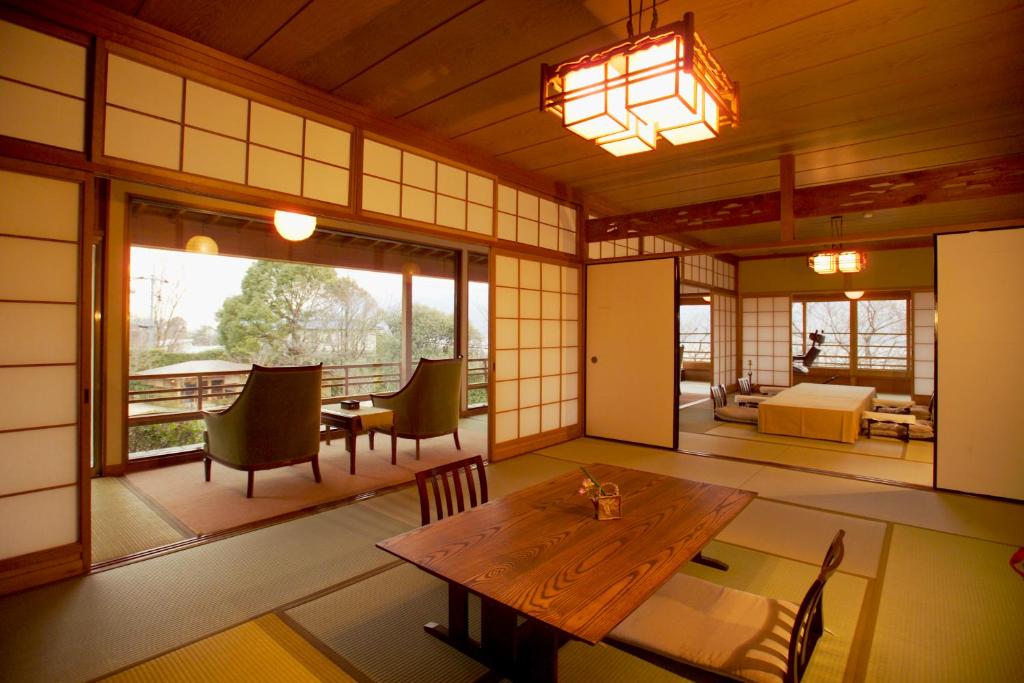Cette chambre dispose d'une grande fenêtre et d'une table avec des chaises en bois. dans l'établissement Sekitei, à Hatsukaichi