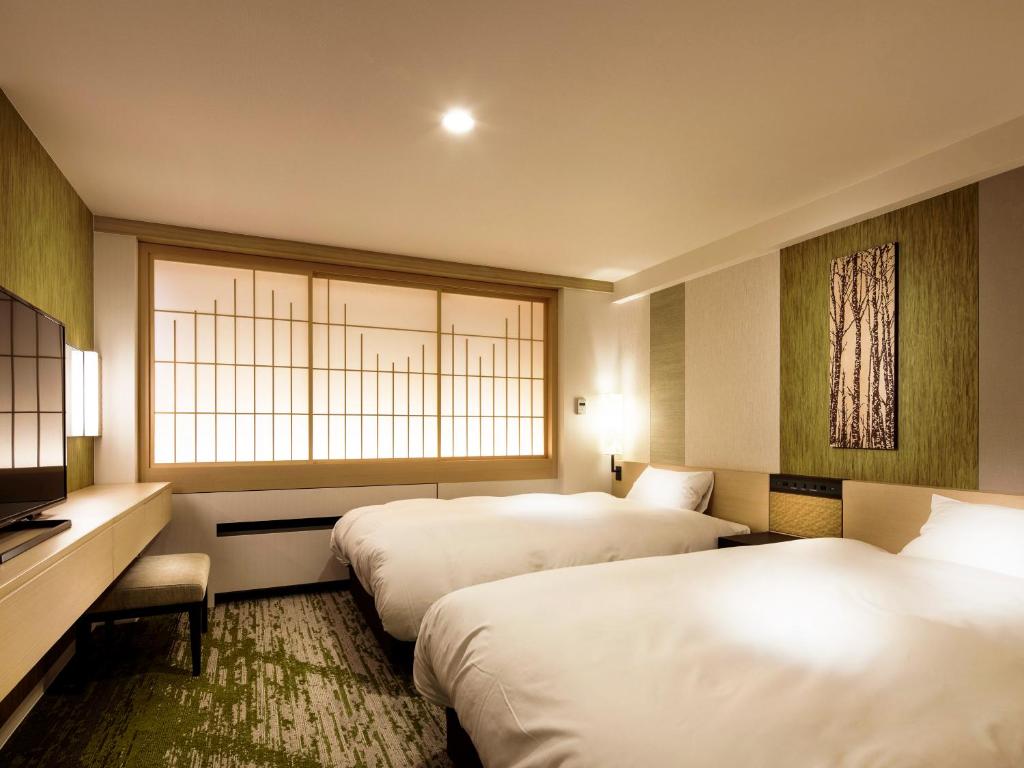 une chambre d'hôtel avec deux lits et une fenêtre dans l'établissement Dai-ichi Takimotokan, à Noboribetsu