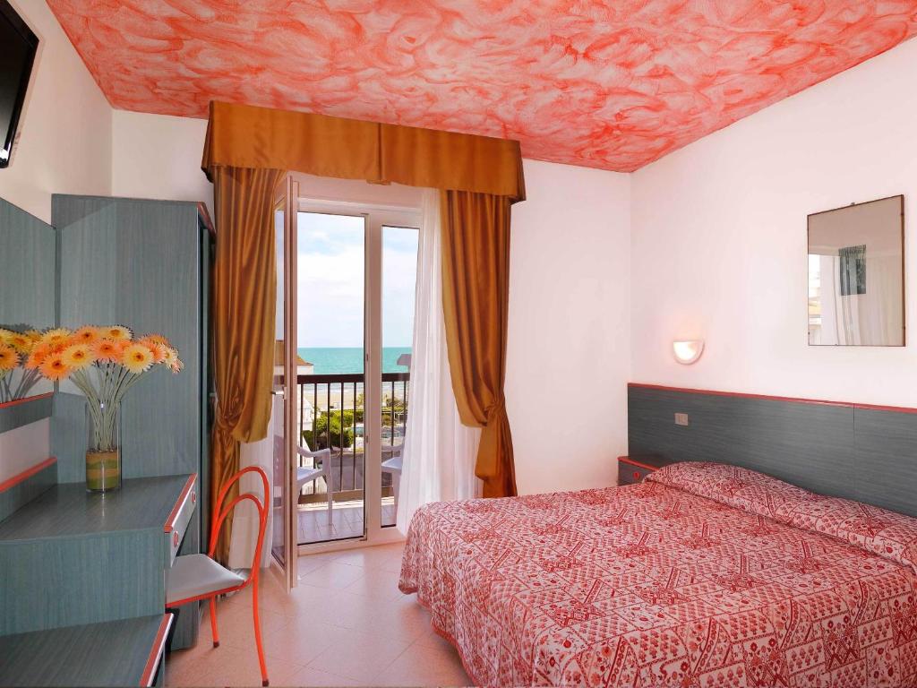 - une chambre avec un lit rouge et un balcon dans l'établissement Hotel Storione, à Lido di Jesolo