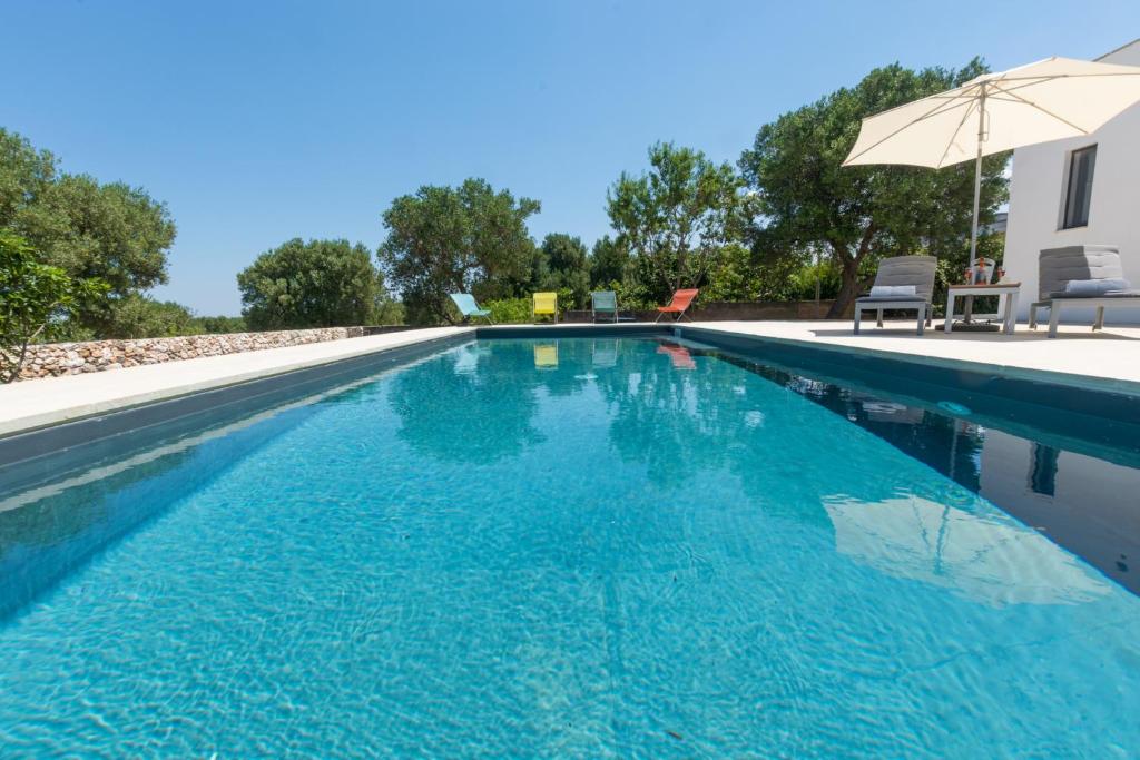 - une piscine d'eau bleue avec un parasol dans l'établissement Villa Roberta by HDSalento, à Specchiolla