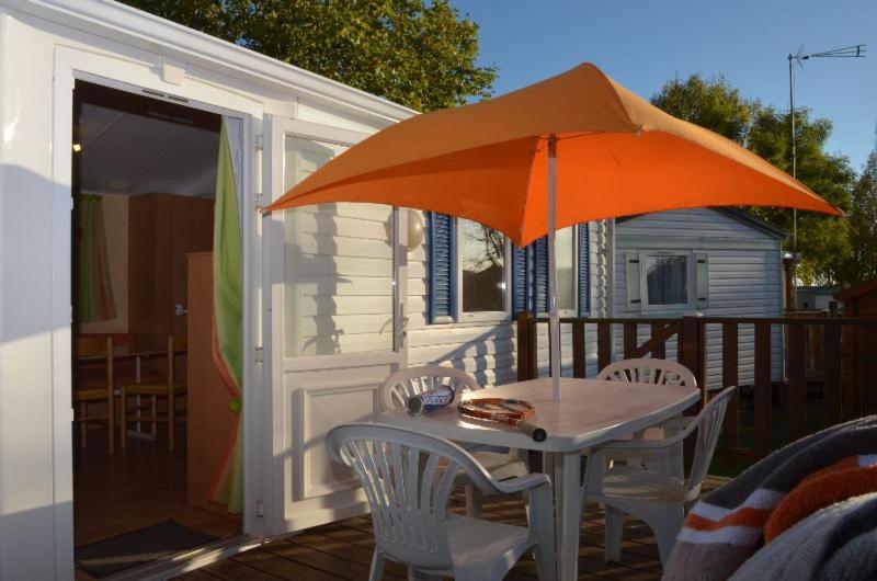 une table et des chaises avec un parasol orange sur une terrasse dans l'établissement Camping Le Puits Rochais, à Les Sables-dʼOlonne