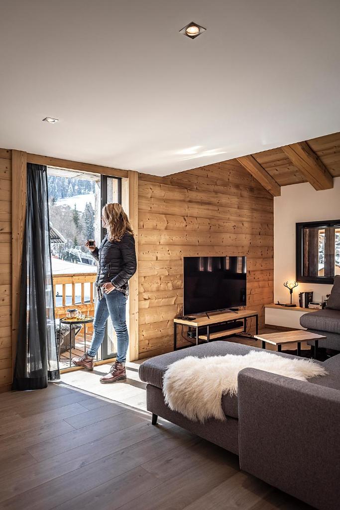 une femme debout dans une pièce donnant par la fenêtre dans l'établissement Spacieux duplex avec vue, à La Clusaz