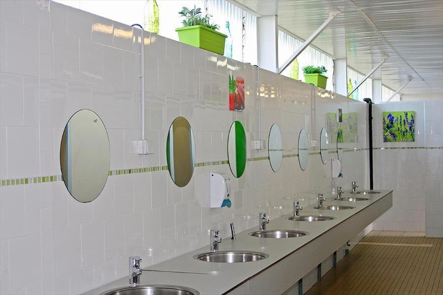 La salle de bains est pourvue d'une rangée de lavabos et de miroirs. dans l'établissement Camping Aux Rives du Soleil, à Pont-de-Vaux