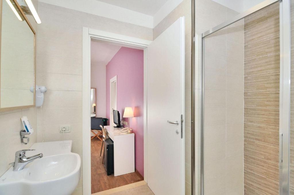 La salle de bains est pourvue d'un lavabo et d'une porte de douche en verre. dans l'établissement Hotel Nederland, à Caorle