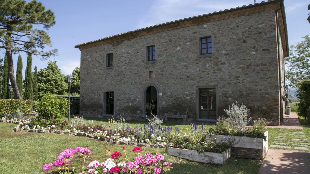 un vieux bâtiment en pierre avec des fleurs devant lui dans l'établissement Le Caselle 26, Emma Villas, à Cortone