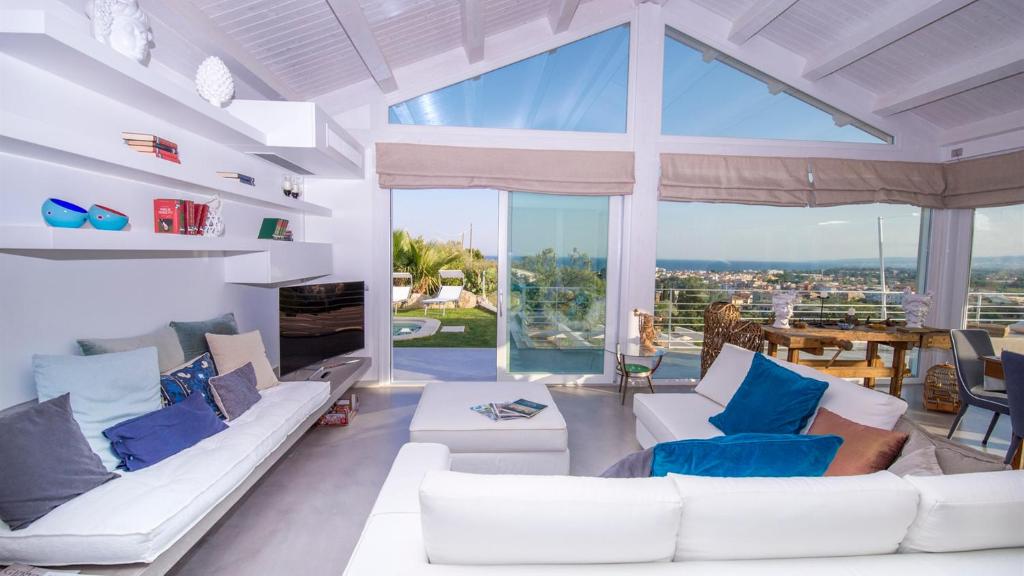 un salon avec des meubles blancs et une grande fenêtre dans l'établissement Villa Aura 6, Emma Villas, à Giardini Naxos