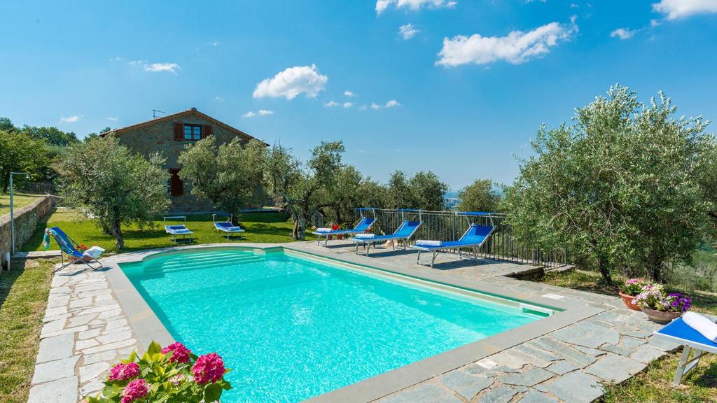 une piscine avec des chaises bleues et une maison dans l'établissement VILLA FABI 6&2, Emma Villas, à Cortone