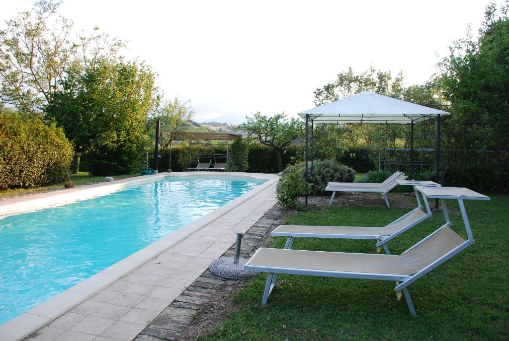 une piscine avec deux chaises longues et un parasol dans l'établissement Casale Iris, à Belmonte Piceno