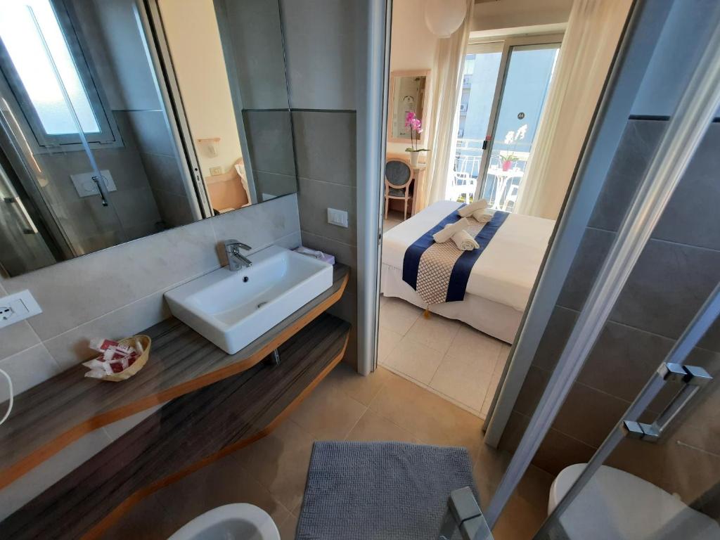 une salle de bain avec un lavabo, un lit et un miroir dans l'établissement Hotel Margherita, à Lido di Jesolo