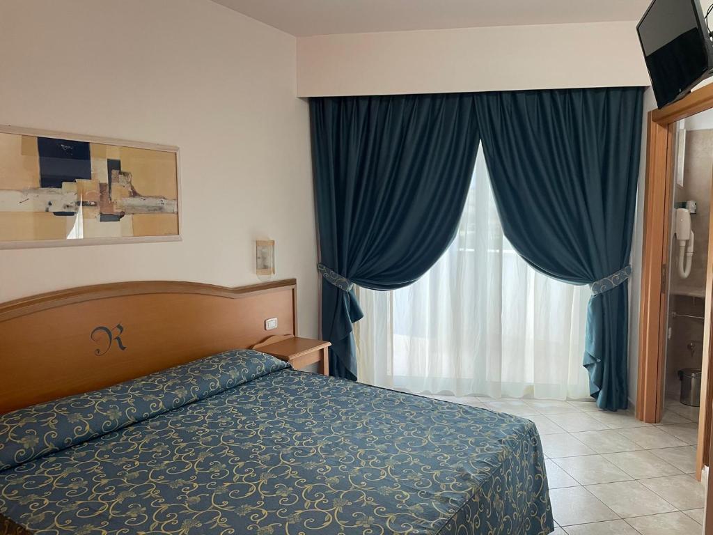une chambre avec un lit et une fenêtre avec des rideaux bleus dans l'établissement Roses Hotel, à Roseto degli Abruzzi