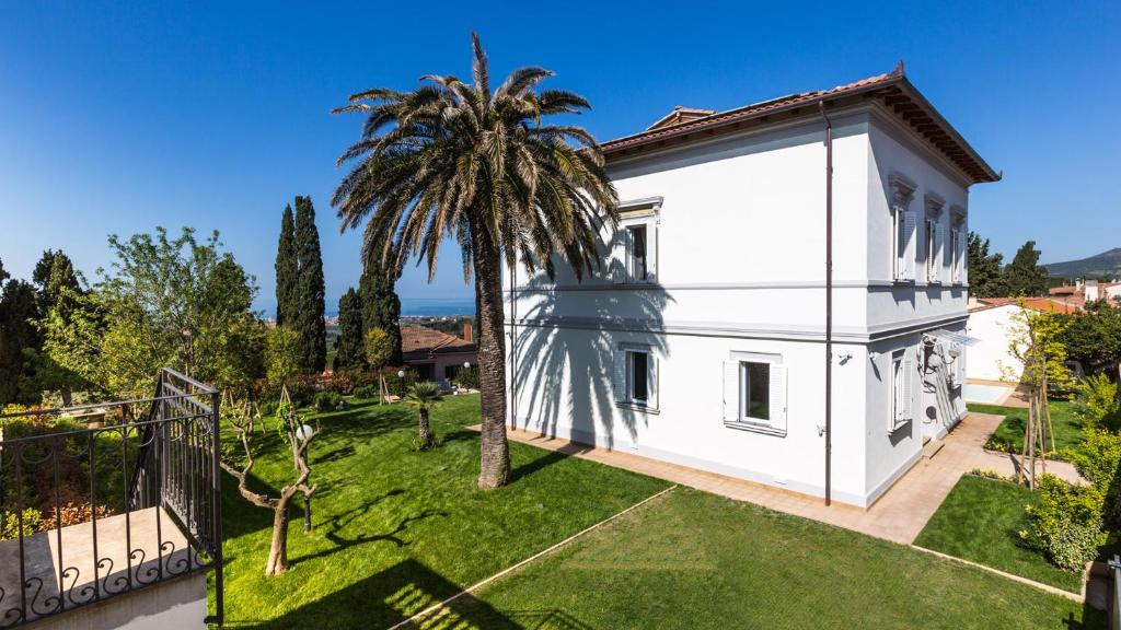 une maison blanche avec un palmier dans une cour dans l'établissement Villa Sole Al Molino A Vento 8, Emma Villas, à Rosignano Marittimo