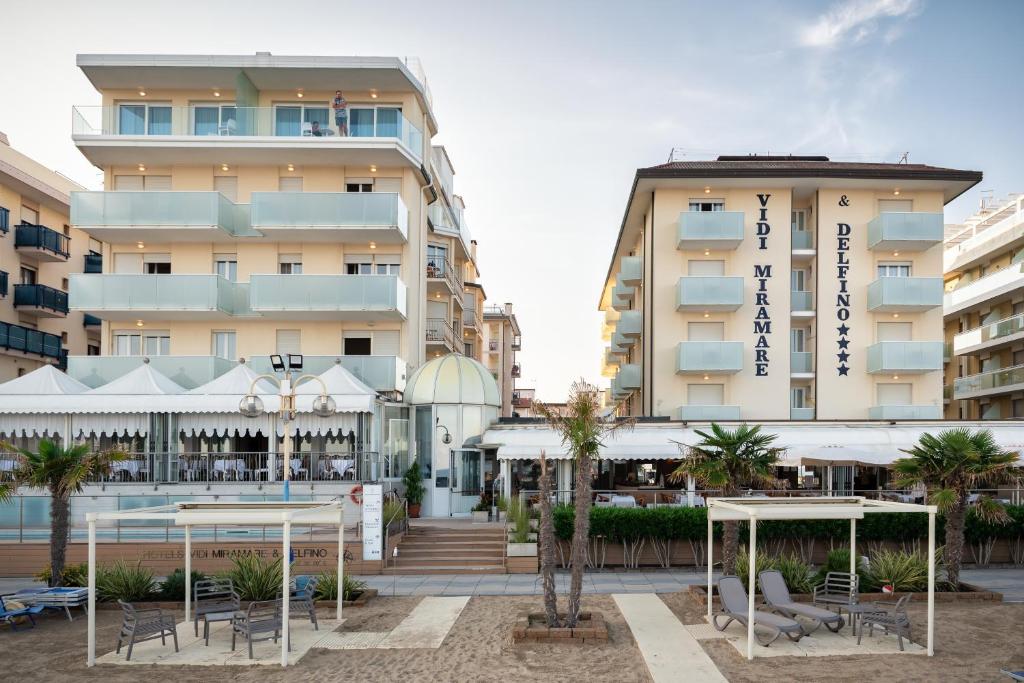 un hôtel avec des tables et des chaises devant un bâtiment dans l'établissement Hotels Vidi Miramare & Delfino, à Lido di Jesolo