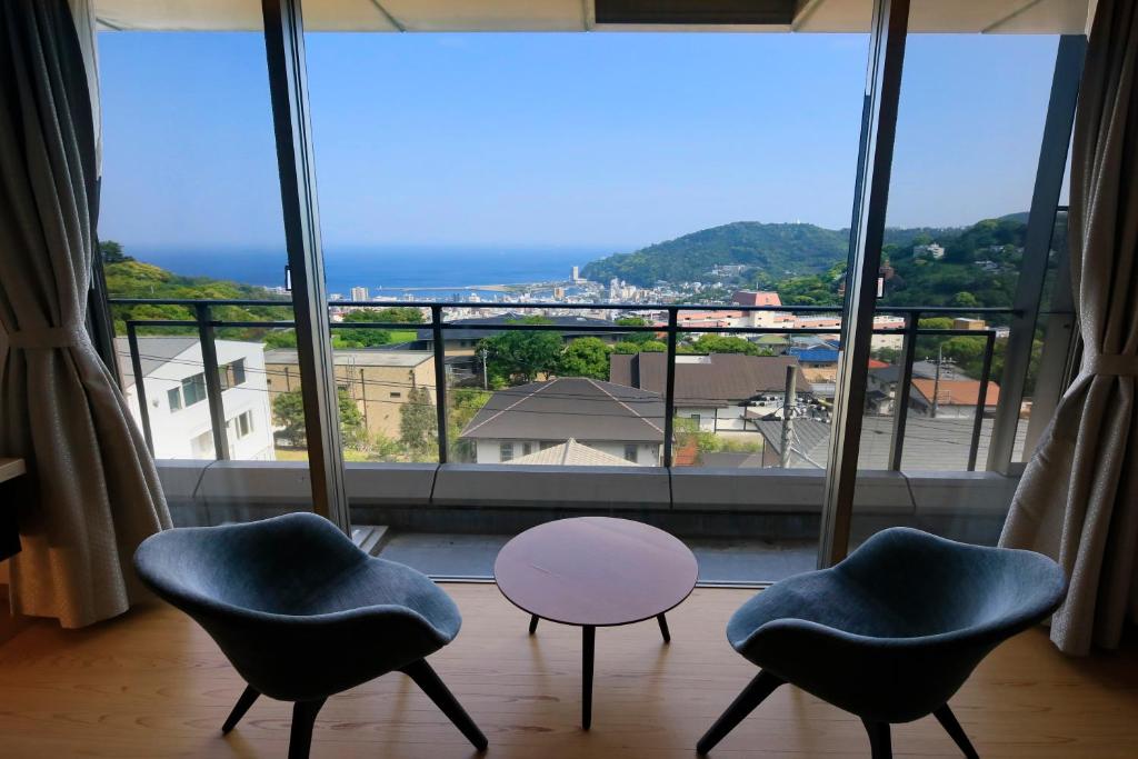 2 chaises et une table devant une grande fenêtre dans l'établissement Atami Fuga, à Atami