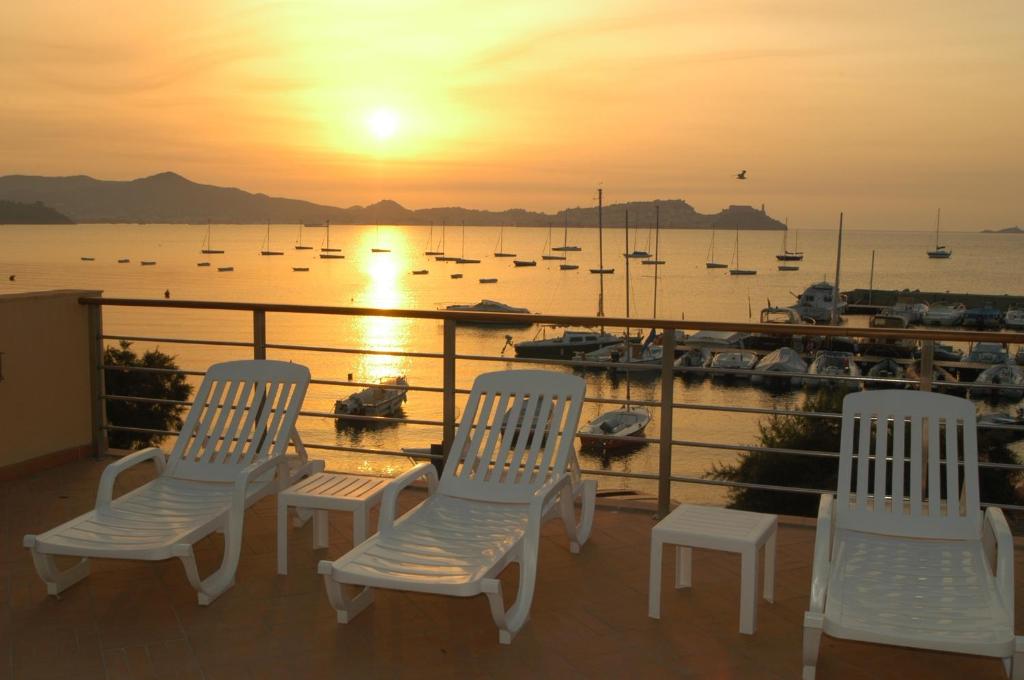 3 chaises blanches assises sur un balcon donnant sur le coucher du soleil dans l'établissement Hotel Mare, à Portoferraio