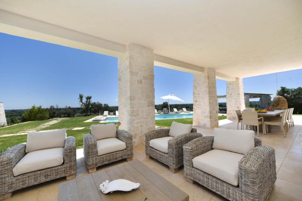 une terrasse avec des chaises en osier, une table et une piscine dans l'établissement Tenuta Lamia degli Ulivi - Ostuni Puglia - Ancient Lamia and Modern Villa, à Ostuni