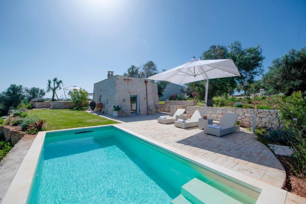 une image d'une piscine dans une cour avec un parasol dans l'établissement Tenuta Lamia degli Ulivi - Ostuni Puglia - Ancient Lamia and Modern Villa, à Ostuni