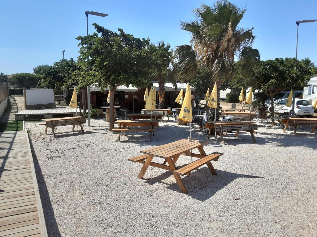 - un groupe de tables de pique-nique et de parasols sur une plage dans l'établissement Mobil home climatisé 5 pers 11210 port la nouvelle, à Port-la-Nouvelle