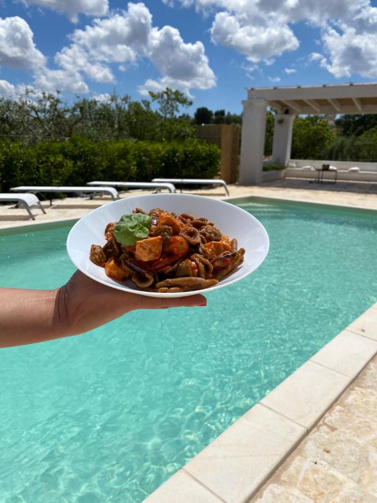 une personne tenant un plat devant une piscine dans l'établissement Casale del Gelso, à Monopoli