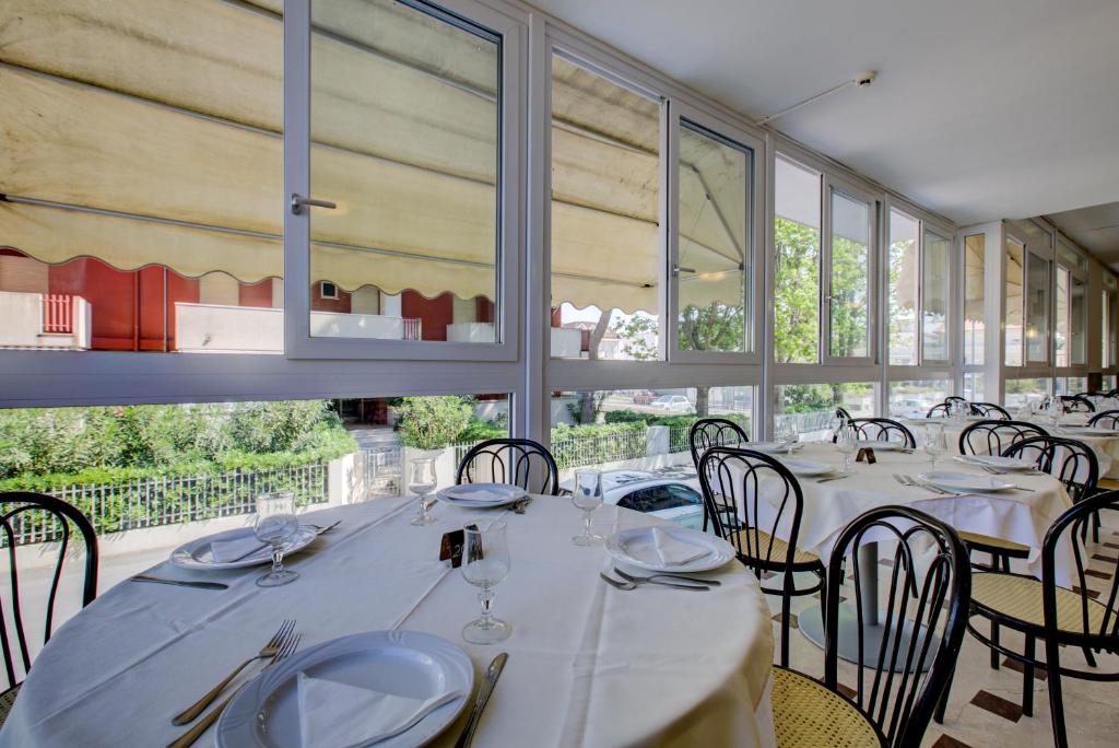 un restaurant avec des tables et des chaises blanches et des fenêtres dans l'établissement Hotel Christian Ideale Per Famiglie, à Riccione