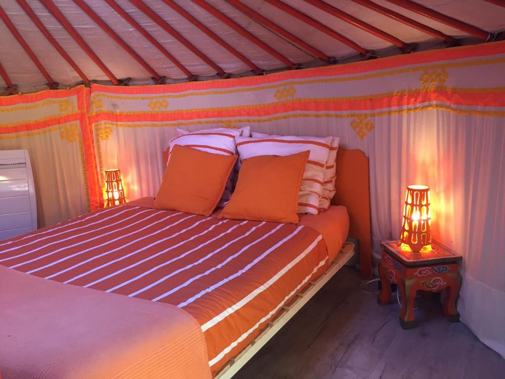 - une chambre avec un lit doté d'oreillers orange et d'une table dans l'établissement Yourte mongole, à Huriel