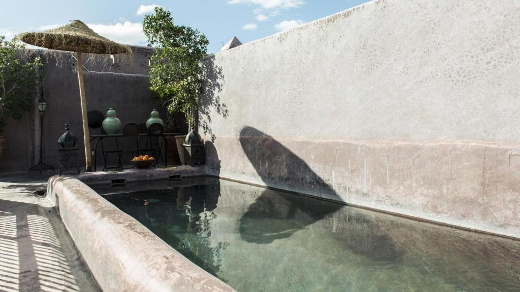 une piscine d'eau à côté d'un mur avec un parapluie dans l'établissement Dar Darma, à Marrakech