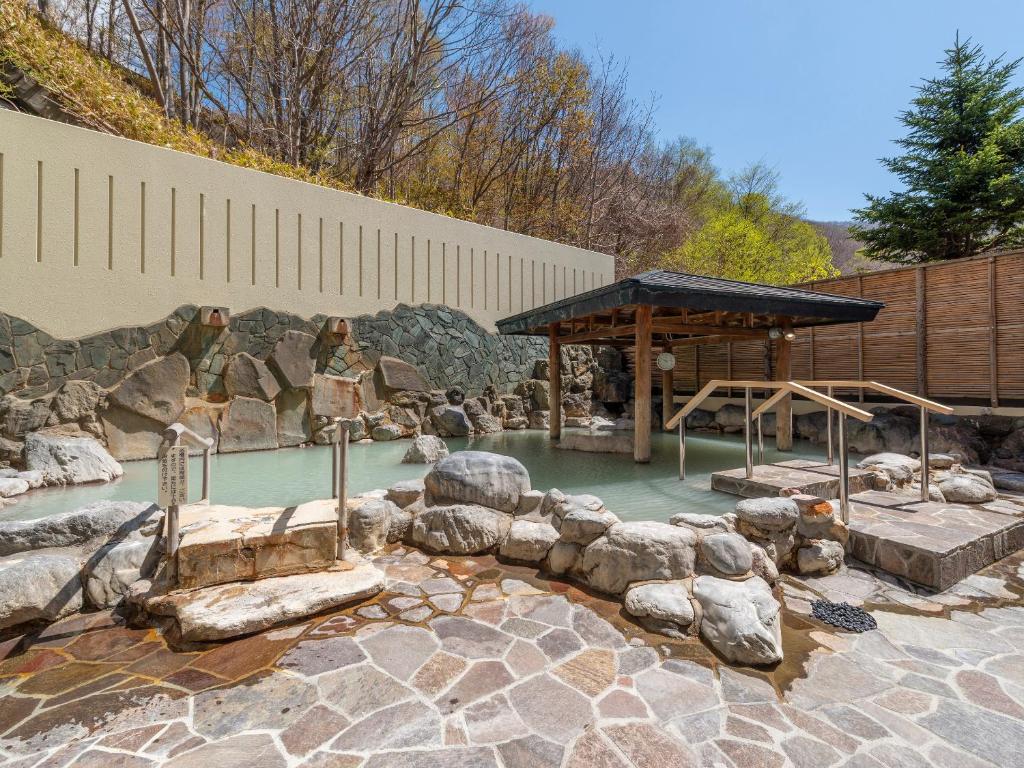 une piscine d'eau avec des rochers et un pavillon dans l'établissement Noboribetsu Manseikaku, à Noboribetsu