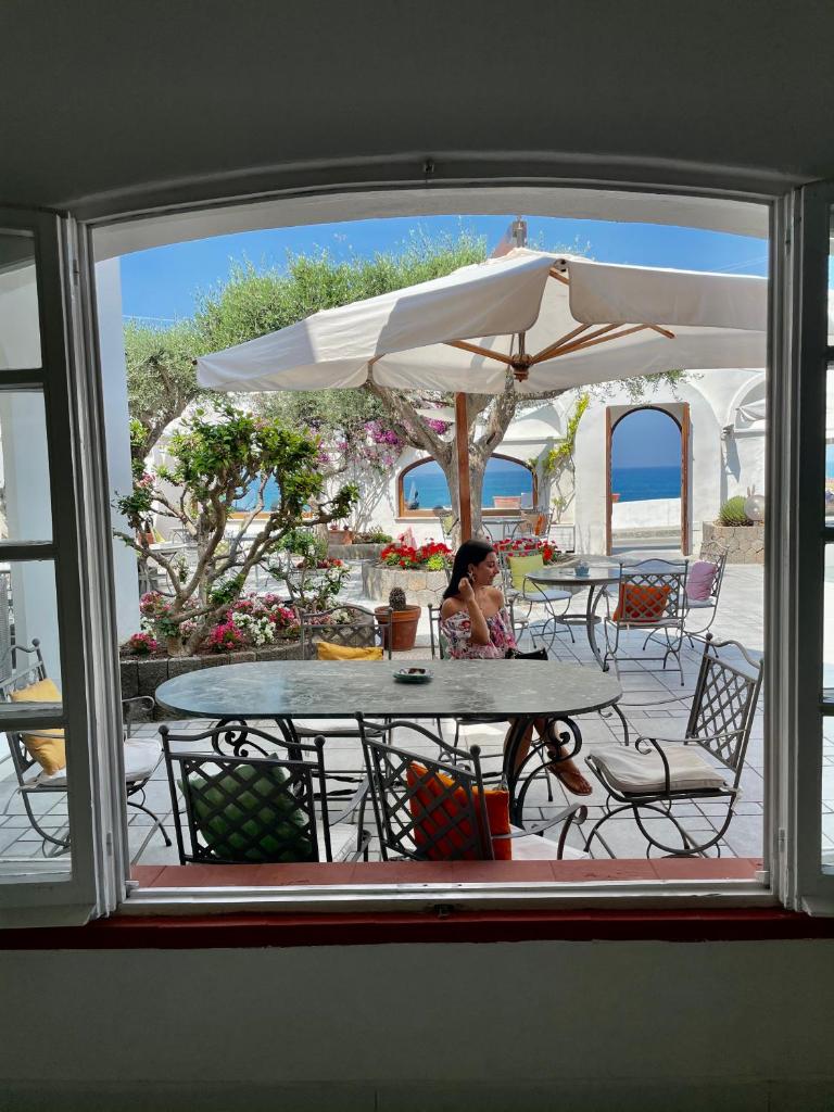 une femme assise à une table avec un parapluie dans l'établissement Hotel La Scogliera, à Ischia