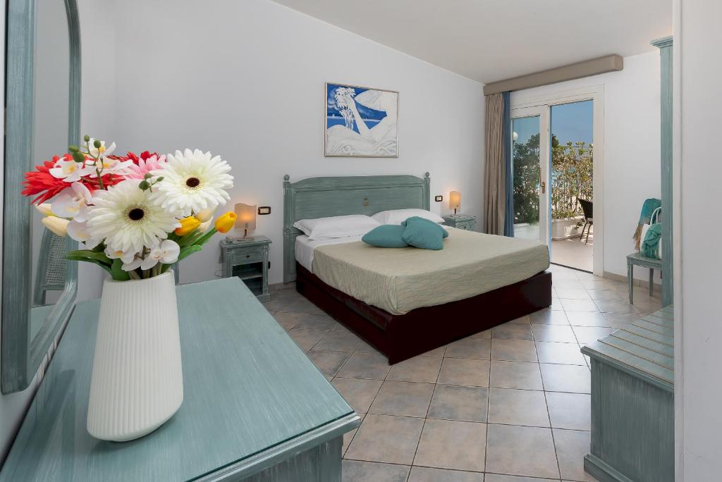 une chambre avec un lit et un vase de fleurs sur une table dans l'établissement Hotel Riviera, à San Vito Lo Capo