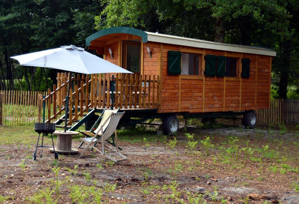 une petite maison avec un parasol, une chaise, une table et un parasol dans l'établissement Roulotte paisible au milieu de la nature, à Sainte-Eulalie-en-Born