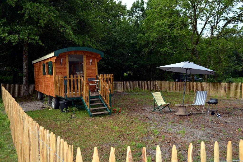 une petite maison dans une cour à côté d'une clôture dans l'établissement Roulotte paisible au milieu de la nature, à Sainte-Eulalie-en-Born