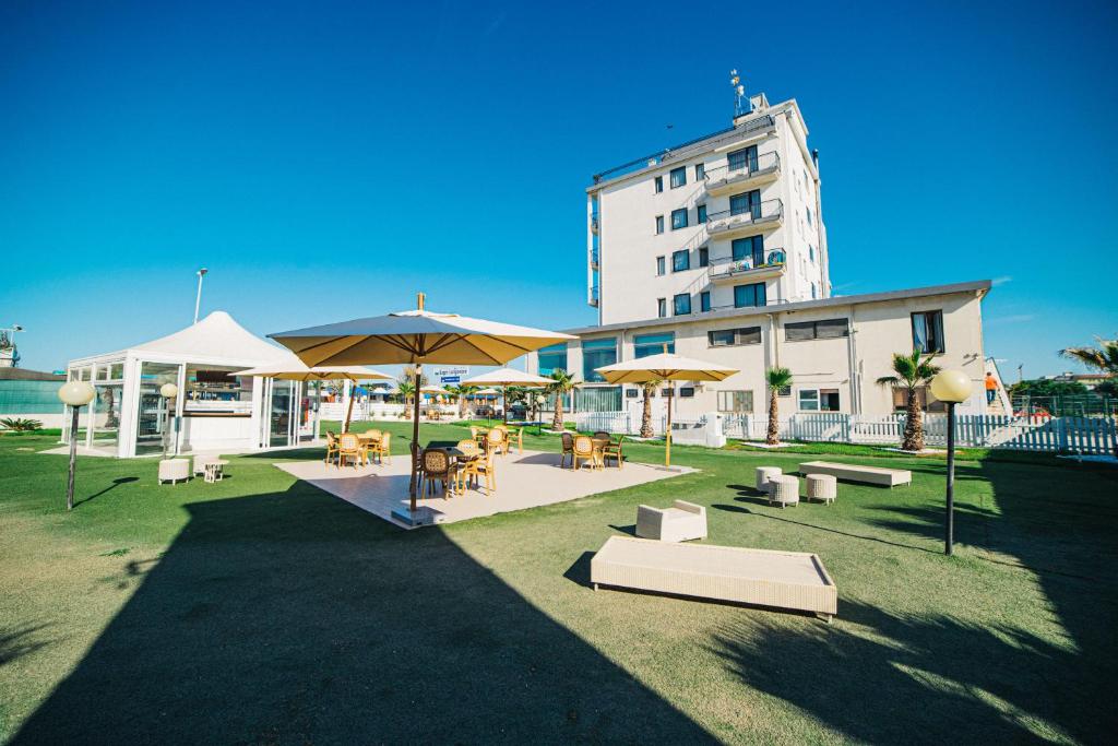 un grand bâtiment avec des tables et des parasols dans une cour dans l'établissement Hotel Park, à Sottomarina
