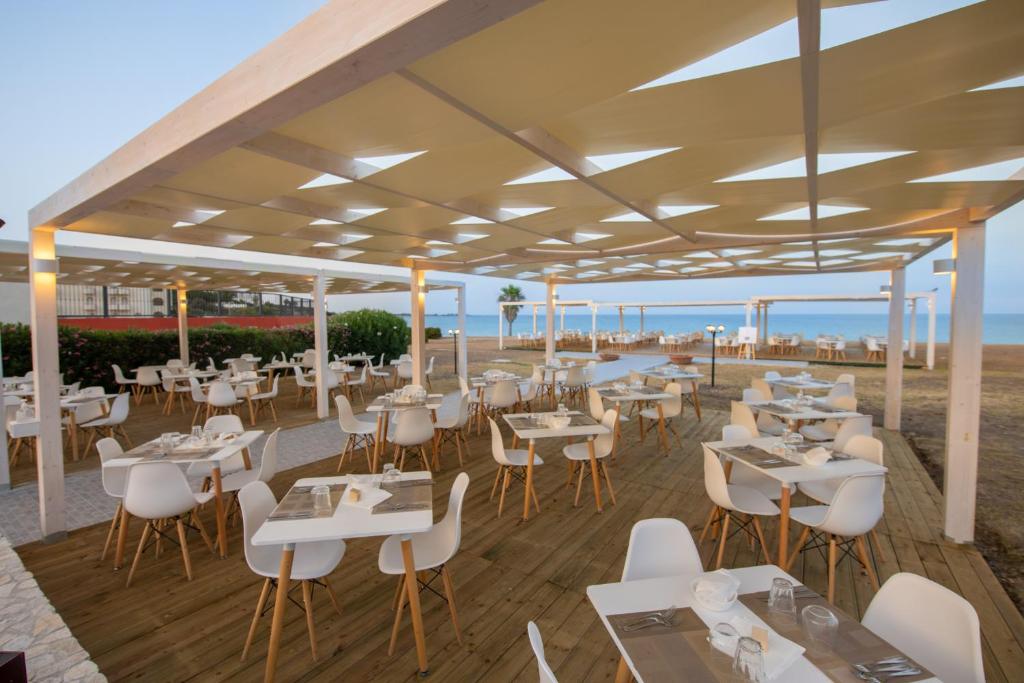 un restaurant sur la plage avec tables et chaises dans l'établissement Hotel Club Eloro, à Noto Marina