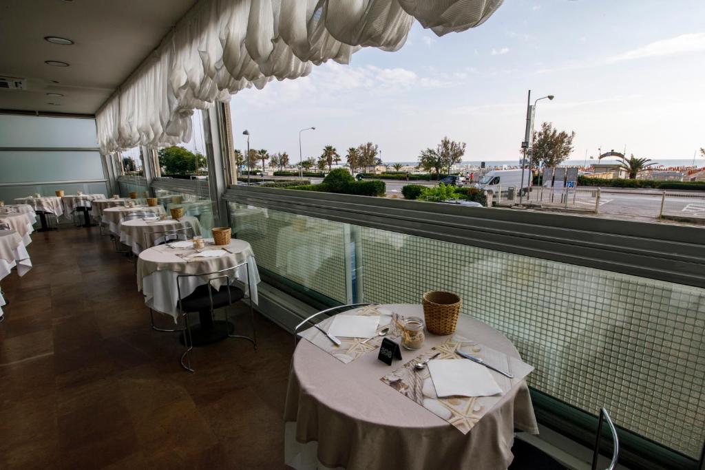 un restaurant avec des tables blanches et une grande fenêtre dans l'établissement Hotel Derby, à Rimini