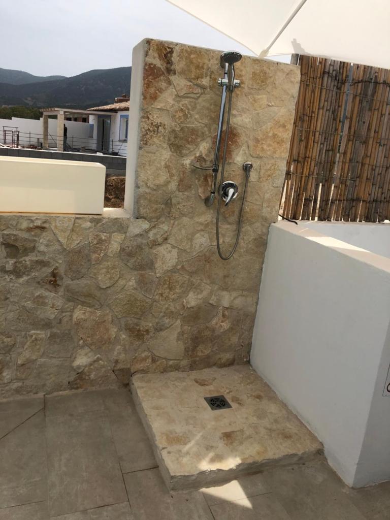 La salle de bains est pourvue d'une douche et d'un mur en pierre. dans l'établissement VILLA AMBRA, à Tertenìa