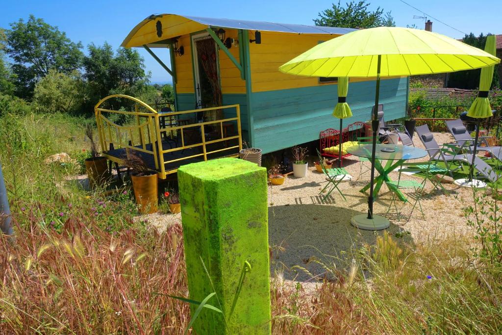un parasol jaune à côté d'une maison avec des chaises dans l'établissement La Ferme De Chenevier, La Roulotte Fleurie 2/4pers, à Saint-Victor