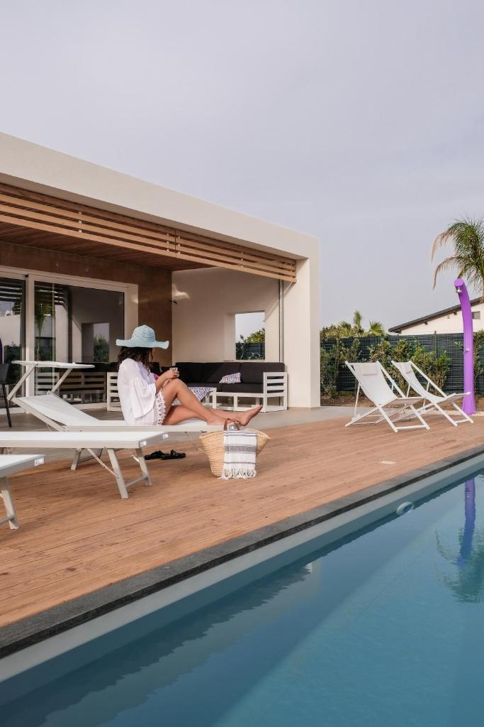 une femme assise sur une chaise à côté d'une piscine dans l'établissement Villa Vannì, à Menfi