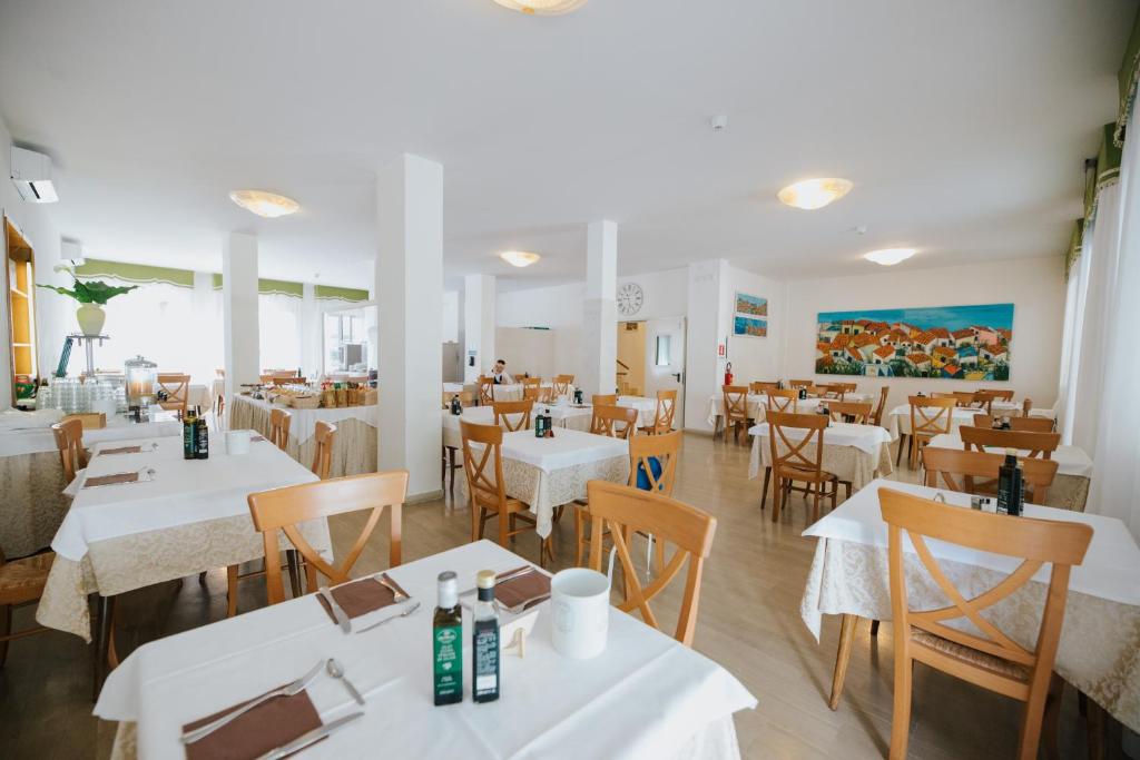 un restaurant avec des tables blanches et des chaises en bois dans l'établissement Hotel Gloria, à Lignano Sabbiadoro