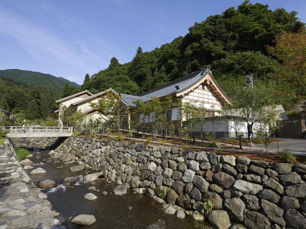 une maison avec un mur en pierre à côté d'une rivière dans l'établissement Hakujukan, à Eiheiji