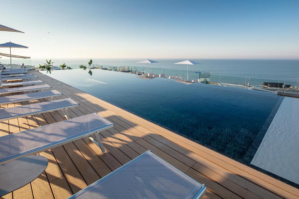 une piscine avec chaises et parasols au bord de l'océan dans l'établissement THE ONE CAORLE - Hotel & Apartments, à Caorle