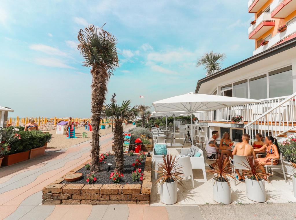 un patio avec des palmiers et des personnes assises à l'extérieur d'un bâtiment dans l'établissement Hotel Loreley, à Lido di Jesolo