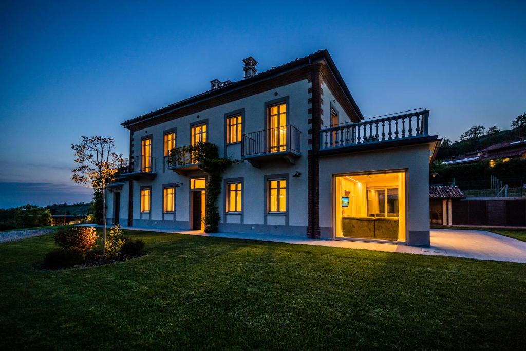 une grande maison blanche avec ses lumières allumées dans l'établissement Villa Leolo' Monforte d'Alba, à Monforte dʼAlba
